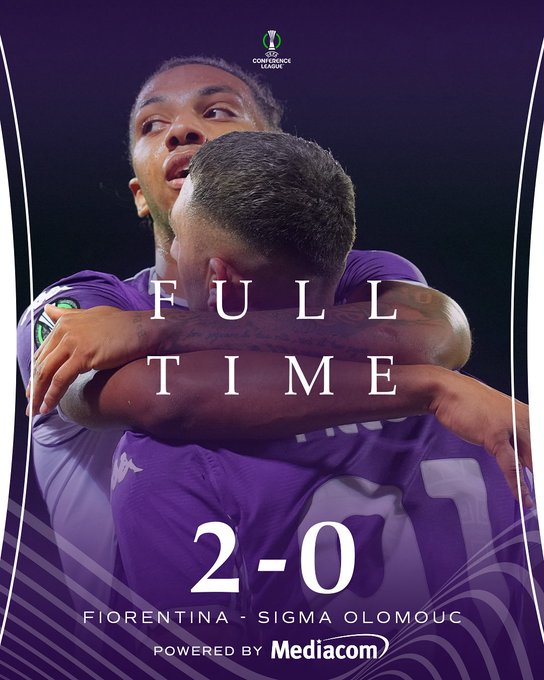 Two soccer players in purple Fiorentina jerseys hugging on a field. The text overlay reads "FULL TIME" and "2-0" with "Fiorentina - Sigma Olomouc" below, indicating the match score.