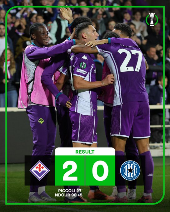 Fiorentina players in purple and white uniforms celebrating on a soccer field, with one player wearing jersey number 27. A crowd is visible in the background. A scoreboard overlay shows a 2-0 result, with "Fiorentina" and "Picolli 37\' N\'Dour 90+5\'" text.
