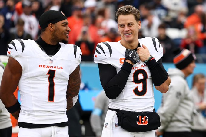 Ja'Marr Chase and Joe Burrow wearing Cincinnati Bengals jerseys. Ja'Marr Chase has the number 1 on his jersey, and Joe Burrow has the number 9. Both are on a football field with a crowd in the background.
