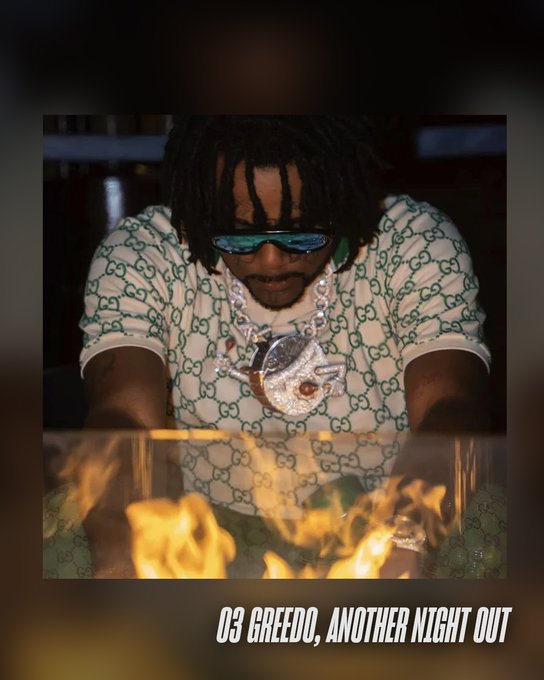 03 Greedo wearing a green Gucci-patterned shirt and large silver chain necklace with a pendant, leaning over flames. Sunglasses cover his eyes, and dreadlocks are visible on his head.