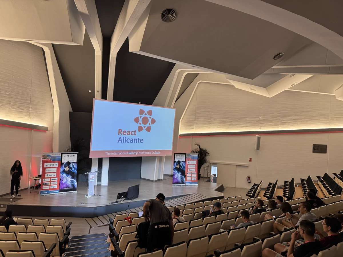Empty conference venue, empty seats, screen shows React Alicante