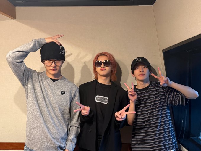 Matsuda Jin, Tajima Shogo, and Takatsuka Daum standing together indoors. Matsuda Jin wears a gray sweater and black beanie, making a peace sign with one hand raised. Tajima Shogo wears a black blazer and sunglasses, also making a peace sign. Takatsuka Daum wears a striped shirt and cap, making a peace sign with both hands.