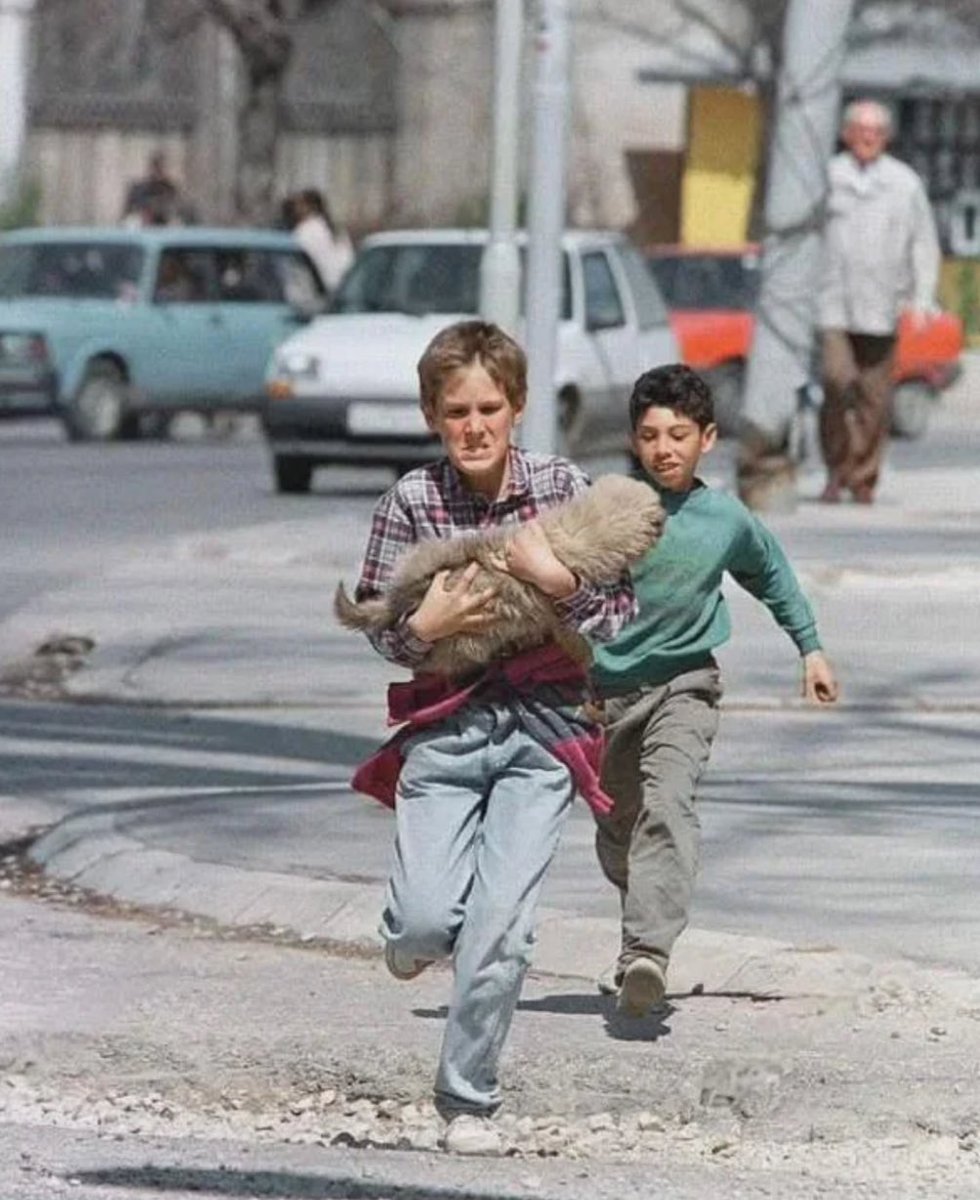MorbidKnowledge's tweet photo. Two boys flee across Sarajevo’s notorious Sniper Alley, clutching their dog. 1995.

According to data gathered in 1995, the snipers wounded 1,030 people and k*lled 225 – 60 of whom were children. https://t.co/FX9RI95XEn