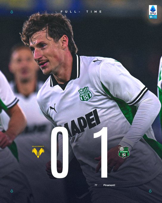 Domenico Berardi wearing a white and green soccer jersey with the Sassuolo logo and MAPEI sponsor. The jersey has black and green accents on the sleeves. The background shows other players in similar uniforms on a field, with text overlays reading "FULL-TIME," "0," "1," and "77 Pinamonti."