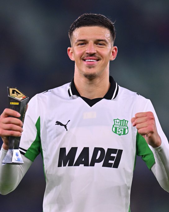 Tarik Muharemović holding a trophy in his right hand, wearing a white and green soccer jersey with "MAPEI" and a logo on the chest, smiling and raising his left fist.
