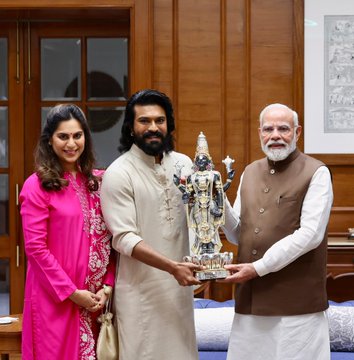 First image shows three people standing in a wooden-paneled room: a woman in a pink saree, a man in a cream kurta holding a silver statue of a deity with a crown, and an elderly man in a beige vest and white kurta, all smiling. Second image depicts three men in a similar room: a long-haired man in cream attire holding one end of a decorated bamboo bow, an elderly man in glasses and beige vest holding the other end, and another man in a light shirt standing beside. Third image features four people seated and standing in the room: woman in pink saree, long-haired man in cream kurta, elderly man in beige vest, and another man in light shirt, with a table and chairs. Fourth image displays a large group of about 15 people on a stage, including men and women in orange and blue sports jerseys with team logos, some in formal attire like white shirts and kurtas, posing with hands raised in celebration.