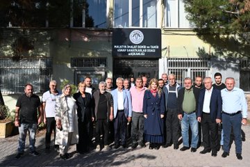 First image shows a large group of about 20 people standing together outside a building with a sign reading Malatya Küçük Sanayi Sitesi, including men and women in business casual attire such as suits, dresses, and headscarves, posing formally on pavement near trees and potted plants. Second image depicts a smaller group of eight individuals outdoors near parked cars and trees, with a woman in a blue coat and scarf gesturing while others in coats and jackets listen attentively. Third image features six people walking on a street lined with trees and buildings, including a woman in a red scarf and blue coat leading, accompanied by men in suits and casual wear. Fourth image portrays an indoor meeting scene with a woman in a blue blazer and red scarf seated at a desk with documents and a salad bowl, flanked by two men in shirts, Turkish and yellow flags on walls, and a large portrait of a man with a quote below.