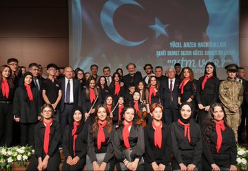 First image shows a man in a dark suit speaking at a podium with microphones from TRT Haber and another outlet, against a backdrop with Turkish flag, text Kim Var, and artist name Yücel Arzen Hacıoğulları, in a hall with chairs and Nevşehir Hacı Bektaş Veli University signage. Second image depicts a group of suited men and women including some in headscarves standing around easels with landscape paintings in a modern glass-walled building. Third image captures a woman in black attire singing into a microphone with hands raised, accompanied by a choir of women in red scarves and black outfits, a man in suit holding a microphone nearby, and a piano on stage in a warmly lit auditorium. Fourth image features a large group of people in black attire with red scarves, some holding violins, posing together on stage with a backdrop of Turkish flag and text about warm family artist Yücel Arzen Hacıoğulları, including military uniform and flowers.