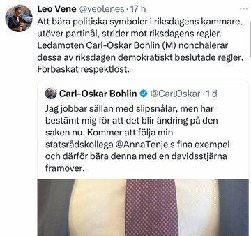 A photo of Carl-Oskar Bohlin wearing a suit and tie with a Davidsstjärna (Star of David) pin on the tie. The background shows a blurred indoor setting, possibly a formal or parliamentary environment.