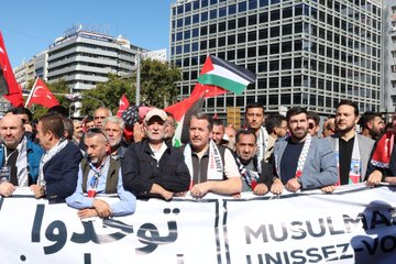 Large crowds holding Turkish and Palestinian flags, standing in an urban square with tall buildings. People carry banners with text in Arabic and Turkish, including "MUSLIMS UNITE" and "GAZZE İÇİN MEYDANLARDAYDIK." Some individuals wear traditional attire, and children hold signs reading "Gazze için dua ediyoruz."