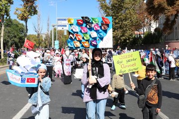 Large crowds holding Turkish and Palestinian flags, standing in an urban square with tall buildings. People carry banners with text in Arabic and Turkish, including "MUSLIMS UNITE" and "GAZZE İÇİN MEYDANLARDAYDIK." Some individuals wear traditional attire, and children hold signs reading "Gazze için dua ediyoruz."