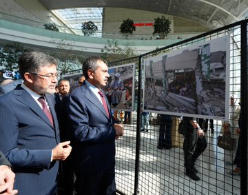 A man speaking at a podium with a backdrop displaying "Eğitimden Bir Kare Fotoğraf Sergisi" and dates 6-12 EYL 2023. Multiple people in formal attire cutting a red ribbon in a spacious indoor area with trees and a glass ceiling. Photographs on display behind a metal fence, including images of children and damaged buildings. Text on banners includes "Millî Eğitim Bakanlığı" and "Gazze".
