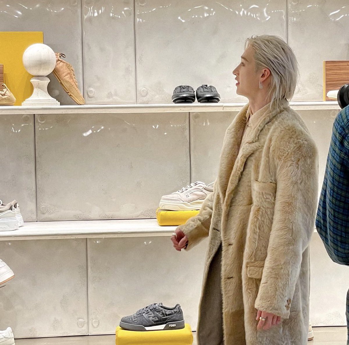 Exuding refined elegance, this figure peruses a chic display of stylish footwear with discerning grace, wrapped in a luxurious fur coat. The sleek, modern setting amplifies the sophisticated allure and fashion-forward vibe.