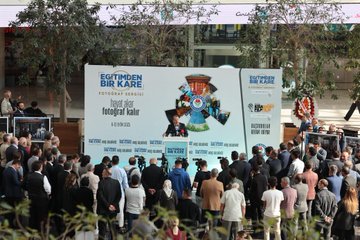 Ali Yalçın speaking at a podium with microphones, addressing a crowd. Yusuf Tekin and İbrahim Yumaklı stand nearby in suits. A large banner displays "Eğitimden Bir Kare Fotoğraf Sergisi" and "Eğitim-Bir-Sen" logo with images. People gather around, some in suits, others casually dressed, near Ankara ATG YHT Gar.