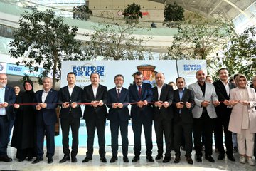 A man in a suit speaking at a podium with a microphone in a spacious indoor area with a modern glass ceiling and greenery. A group of people in formal attire stands behind him, some holding a red ribbon. Banners display "Eğitimden Bir Kare" and logos, with photographs of people in distress visible on display boards. Another image shows a group of people in suits cutting a red ribbon in front of a banner with "Eğitimden Bir Kare" and images of people in distress. Additional photos show men in suits observing photographs on display boards.