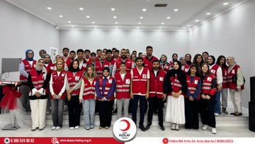 First image shows a conference room with participants seated around tables wearing red vests some standing and one woman presenting in front of a projector screen displaying Turkiye Afet Müdahale Ekip with Turkish Red Crescent logo visible on screen and tables. Second image depicts a larger group of people in red vests seated at round tables in a spacious hall with beverages on tables and the Turkish Red Crescent logo on a banner. Third image features a group photo of diverse participants including men and women in red vests standing together in a room with the Turkish Red Crescent logo on a banner behind them. Watermarks from Düzce Kızılay appear on all images.