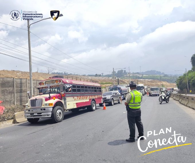 Una escena de carretera muestra un autobÃºs rojo y blanco estacionado en el lado derecho con varios vehÃ­culos como autos y una motocicleta detenidos detrÃ¡s de conos naranjas reflejantes. Un oficial de seguridad con chaleco amarillo fluorescente y sombrero estÃ¡ de pie en el centro de la carretera dirigiendo el trÃ¡fico con una mano extendida. En el fondo hay una cerca de malla con tierra excavada y vegetaciÃ³n en una colina bajo un cielo parcialmente nublado. Postes de luz y cables de energÃ­a corren a lo largo del lado izquierdo de la carretera. Logos superpuestos incluyen escudos de ministerios guatemaltecos y un emblema de Provial en la esquina superior izquierda. Texto amarillo en la imagen dice PLAN CONECTA en la parte inferior.