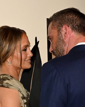First image shows Jennifer Lopez in a green floral dress with black fabric elements leaning close to Ben Affleck in a suit, both smiling at each other against a neutral background. Second image depicts Jennifer Lopez posing alone on a red carpet backdrop labeled Kiss Of The Spider Woman screening, wearing a sheer green gown with large black circular accents around the neckline and midsection, floral patterns visible, standing confidently. Third image captures Jennifer Lopez in a backless green top and skirt with black overlay embracing Ben Affleck from behind, both looking affectionate near a wall.