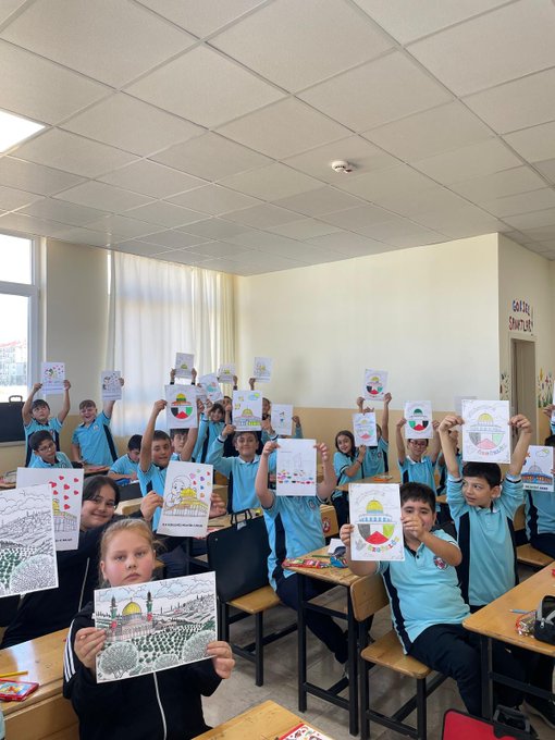 First image shows group of schoolchildren in blue uniforms standing in classroom holding up colorful drawings including sun, hearts, landscapes, and Al-Aqsa Mosque structure on white paper with crayons. Second image depicts students around desk with Palestinian flag held up, Turkish flag, banner reading Filistin için dua ediyoruz, and poster with heart and Palestinian flag colors. Fourth image displays multiple handmade paper crafts resembling Palestinian keffiyehs with black and white patterns, red green white ribbons hanging from them arranged on gray surface.