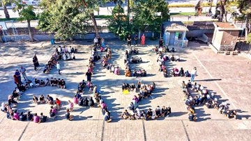 First image shows a school courtyard with students in uniforms standing in groups holding large Palestinian and Turkish flags, surrounded by buildings, trees, and a basketball hoop. Second image depicts students sitting on the ground forming the word FİLİSTİN with their bodies in the courtyard amid trees and structures. Third image captures students seated forming the word GAZZE on the paved school yard with a Turkish flag on a pole nearby and vehicles in the background. Fourth image features a school building with a dome, trees, and students in red and blue uniforms gathered in the courtyard under sunny skies.