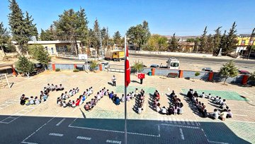 First image shows a school courtyard with students in uniforms standing in groups holding large Palestinian and Turkish flags, surrounded by buildings, trees, and a basketball hoop. Second image depicts students sitting on the ground forming the word FİLİSTİN with their bodies in the courtyard amid trees and structures. Third image captures students seated forming the word GAZZE on the paved school yard with a Turkish flag on a pole nearby and vehicles in the background. Fourth image features a school building with a dome, trees, and students in red and blue uniforms gathered in the courtyard under sunny skies.