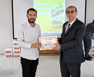 First image shows four men in suits seated at a wooden table in a meeting room with Turkish flags, holding microphones, glasses of tea, water bottles, and plates with pastries, branded boxes labeled ANA ARI on the table, wooden wall background. Second image depicts eight men in formal attire sitting around a long wooden table in a modern room with wooden walls, spotlights, and flags including Turkish and another national flag, plates and cups on the table. Third image features two men, one in white shirt and one in suit, standing on a stage holding a certificate framed with yellow border, projector screen displaying ANA ARI YETISTIRICILIGI in yellow and green, stacks of white boxes nearby on the floor. Fourth image displays a large group of about 20 diverse individuals including men and women in various attire like suits, abayas, and casual clothes, standing in a semi-circle in a spacious hall with white walls, ceiling lights, and Arabic signage, many holding certificates.