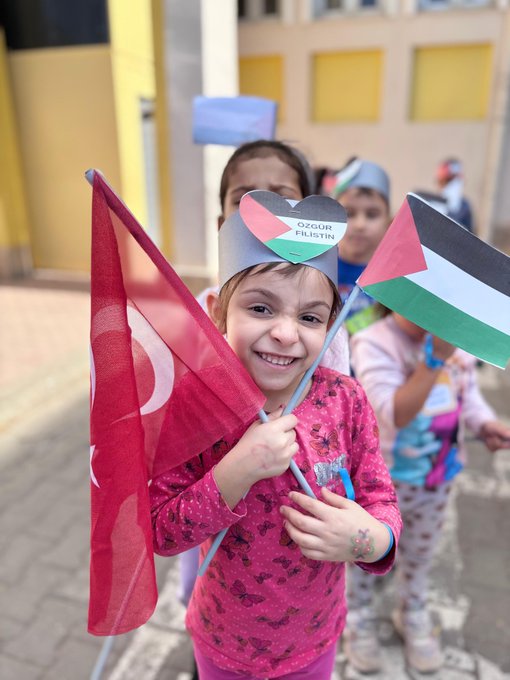 First image shows group of schoolchildren in uniforms standing on steps of yellow building with Golkent Okulu sign, holding white papers or drawings, adults nearby. Second image depicts young girl in pink dress smiling while holding Turkish flag, wearing paper hat, surrounded by children with Palestinian flags. Third image features yellow banner reading Her yer yer Gazze her yer direnis held by man in yellow hoodie, people with Palestinian and Turkish flags in background under blue sky. Fourth image captures large group of students and adults in school yard waving Turkish and Palestinian flags, some holding yellow banners, green building and trees visible.