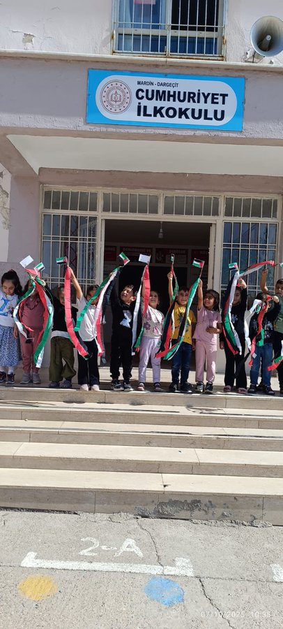 First image shows the front of a school building with a blue sign reading CUMHURIYET ILKOKULU and the Turkish flag emblem, children in colorful clothing standing on steps holding and waving Palestinian and Turkish flags. Second image depicts children on a sunny outdoor playground running and playing with Palestinian flags, some barefoot, against a background of school buildings and trees. Third image features a girl coloring a detailed drawing of Palestinian map, Dome of the Rock, ships, tents, and the number 68 on a checkered table with crayons, pencils, a water bottle, and toys nearby. Fourth image shows another girl at a table cutting or coloring a similar artwork with Palestinian symbols, ships, a girl in headscarf, flags, and landmarks on a blue mat with school bags and supplies around.