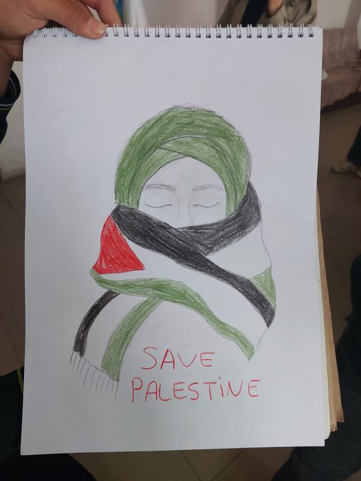 First image shows a child with curly hair sitting at a wooden desk in a classroom, drawing on white paper with a black marker, surrounded by colored pencils, crayons, notebooks, and a green pencil case; the paper has handwritten text in Turkish reading Filistin and Filistin bayrağı, with a partial Palestinian flag design visible. Second image depicts a classroom with students seated at desks watching a smartboard displaying a video titled Filistin with cityscape visuals, a framed portrait on the wall, and children in school uniforms attentively viewing. Third image features a hand holding a notebook page with a colored pencil drawing of a womans face wearing a green headscarf and black and white scarf resembling the Palestinian flag colors, accompanied by red handwritten text Save Palestine. Fourth image shows a close-up of a white paper with a pencil sketch of a raised fist wearing a green and red bracelet in Palestinian flag colors.