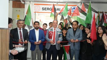 First image shows a large group of students and teachers standing in front of Şehit Fatih Doğan Güzel Sanatlar Lisesi building with a banner reading Adıyaman Şehit Fatih Doğan Lisesi, holding Turkish and Palestinian flags and a large banner stating Soykırıma Hayır Filistin’e Destek Siyonizme Lanet. Second image depicts Provincial Director Ali Tosun wearing a scarf with Turkish and Palestinian flag colors in an art gallery space surrounded by students in headscarves and traditional attire viewing framed artworks including Palestinian flag motifs and landscape paintings. Third image captures a ribbon-cutting ceremony at an entrance with Turkish and Palestinian flags, participants in suits and traditional clothing holding scissors over a red ribbon, with a sign reading Sergi Salonu. Fourth image features a group of diverse participants including men women and youth in casual and formal attire standing on a red carpet in an exhibition hall holding Palestinian flags, surrounded by framed artworks and portraits with Palestinian themes.