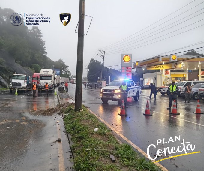 First image shows a misty road scene with a police vehicle with lights on parked near a Shell gas station on a highway. Workers in orange vests and traffic cones manage several trucks and vehicles on a wet road with green hills in the background. A yellow text overlay reads PLAN Conectate. Second image depicts a foggy mountainous road with construction equipment including a yellow excavator and bulldozer clearing debris from a landslide area. Police officers in blue uniforms stand near a white police SUV with cones and barriers set up along the wet asphalt road with trees and a white tent nearby. A yellow text overlay reads PLAN Conectate.