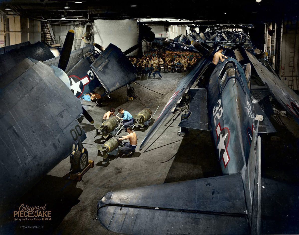 Crew ready bombs beside Grumman F6F Hellcats aboard USS Yorktown CV-10, while part of the crew watches a movie, Pacific Ocean, 1944.

Colourised PIECE of JAKE