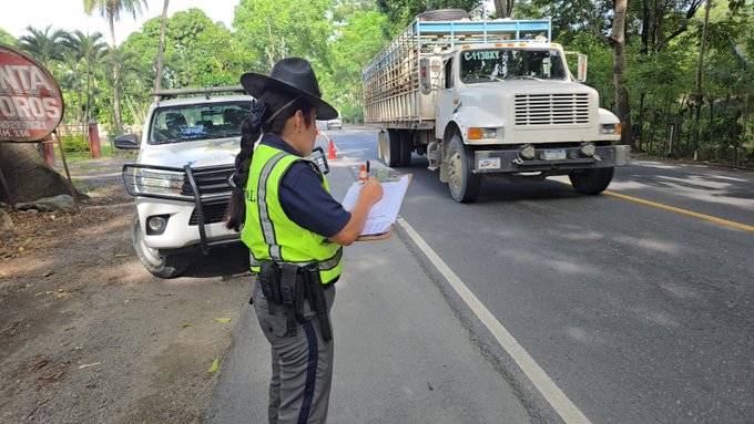 Primera imagen muestra a una oficial de trafico con uniforme azul y chaleco reflectante amarillo sosteniendo un portapapeles y sombrero negro parada en una carretera rodeada de vegetacion tropical y palmeras con un camion de carga blanco con remolque azul estacionado al lado y un vehiculo blanco al fondo junto a un letrero rojo que dice SANTA. Segunda imagen muestra un vehiculo utilitario blanco con logo PROVIAL y equipo de trafico amarillo estacionado en una carretera con arboles verdes a los lados conos naranjas de trafico colocados en la via y un camion al fondo en un area rural sombreada.