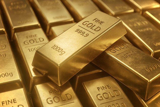 Multiple rectangular gold bars stacked together, each engraved with FINE GOLD and weights such as 1000g or 999.9, arranged in a close-up view on a reflective surface showing metallic shine and precise engravings.