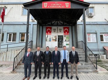 First image shows three men in suits standing in an office with Turkish flags, a framed portrait of Mustafa Kemal Atatürk on the wall, a large screen displaying the Turkish flag, bookshelves, and a wooden desk; one man holds a plaque with the Turkish flag emblem. Second image depicts six people including a woman in an orange top and men in suits posing in front of a large screen with the Turkish flag, a portrait of Atatürk, office chairs, and a door; flags and a framed emblem are visible on shelves. Third image features seven men in suits standing on steps in front of a government building entrance with a sign reading Çukurca Kaymakamlığı, Turkish flags on poles, and architectural elements like columns and windows.