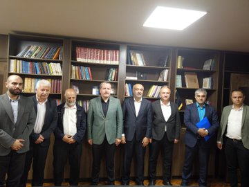 First image shows a group of formally dressed men and women standing around a conference table holding documents, with flags of Uzbekistan, Germany, and Turkey on the table adorned with flowers and tissues in a well-lit room. Second image depicts several men in suits seated around a wooden table with food plates, drinks, and portraits of bearded men on the wall in a paneled room. Third image features a group of men in suits standing in front of wooden bookshelves filled with books in a library-like setting. Fourth image displays a modern gray building exterior with a green circular emblem labeled Maarif Schools Baghdad Mansour Campus, and a group of suited men standing in front of the entrance.