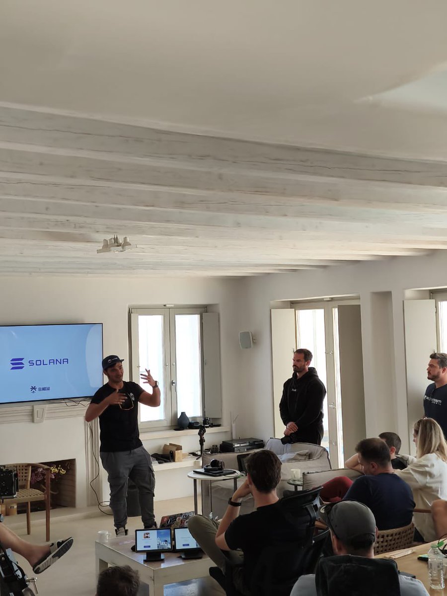 Presenter at Island DAO Mykonos gesturing during a talk on DAO incorporation, with participants seated and Solana branding in the background