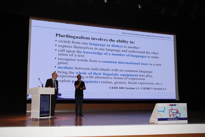 İlk görüntüde büyük bir ekran Plurilingualism involves the ability to use multiple languages veya dillerini kullanma yeteneğini içeren plurilingualism başlığı altında sunum gösteriyor ve iki konuşmacı sahne önünde duruyor. İkinci görüntüde bir konferans salonu kalabalık izleyici koltukları Türk bayrakları ve sahnede moderatör ile panelistler Yabancı Dil Eğitimi in CEFR başlığı altında tartışma yapıyor. Üçüncü görüntüde Dr Nihat ve Dr Nazlı Görgöz isimleri yazılı grup fotoğrafı çeşitli katılımcılar sahne önünde poz veriyor renkli grafik unsurlarla süslenmiş arka plan.