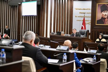 First image shows five men in suits seated at a long white table in a modern room with a gold AK Parti emblem on the wall and Turkish flag; they appear to be in a formal discussion with microphones and documents. Second image depicts two men in suits sitting in a conference hall with multiple flags including Turkish and others on tables and podiums surrounded by audience members. Third image captures a group of about twenty men and women in business attire seated in rows of chairs in a brightly lit room with a photographer visible. Fourth image illustrates a formal assembly in a wooden-paneled room with a large portrait of Mustafa Kemal Atatürk a Turkish flag and participants at desks with laptops and water bottles discussing under a screen.