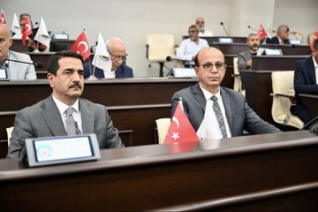 First image shows five men in suits seated at a long white table in a modern room with a gold AK Parti emblem on the wall and Turkish flag; they appear to be in a formal discussion with microphones and documents. Second image depicts two men in suits sitting in a conference hall with multiple flags including Turkish and others on tables and podiums surrounded by audience members. Third image captures a group of about twenty men and women in business attire seated in rows of chairs in a brightly lit room with a photographer visible. Fourth image illustrates a formal assembly in a wooden-paneled room with a large portrait of Mustafa Kemal Atatürk a Turkish flag and participants at desks with laptops and water bottles discussing under a screen.