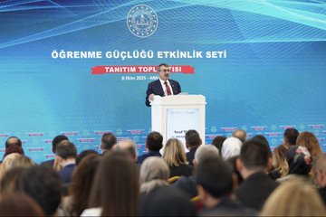 First image shows a large Turkish flag backdrop in a conference hall with rows of formally dressed men standing attentively on a blue stage area. Second image depicts a man in a suit speaking at a podium with a banner reading Ögrenme Güclüü Etkinlik Seti Tanim Toplantisi and the date 5 Ekim 2023 behind him, audience seated in front. Third image features a group of adults and children in formal attire holding musical instruments like flutes and clarinets, standing in front of a Turkish emblem on a wall. Fourth image displays two colorful boxed sets of educational materials labeled ÖGES for learning difficulty awareness series, with illustrated children and books on a table.
