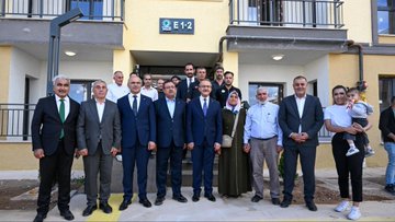 First image shows six men in suits and one in a black shirt with APAD patch standing behind a podium with microphones and MHP logo during an outdoor press event in an urban setting with buildings and flags. Second image depicts a group of men in suits and casual attire including one holding a microphone with Turkish flag pin and APAD shirt in a similar outdoor gathering with buildings in background. Third image features men in suits and a woman in headscarf with a young girl in yellow dress holding keys and a laptop in front of apartment buildings. Fourth image displays a large group of men and women in formal and traditional attire including suits headscarves and a baby in front of a yellow apartment building entrance labeled E12.