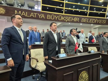 First image shows group of men in suits seated around wooden conference table in room with Turkish flags, white flags, portraits of Mustafa Kemal Atatürk and Recep Tayyip Erdoğan on walls, air conditioning unit visible, formal meeting setting. Second image depicts diverse group including men and one woman in business attire seated in rows on chairs against white wall with radiator, lit room suggesting assembly or seminar. Third image captures tiered assembly hall with wooden paneling, Malatya Büyükşehir Belediyesi sign, multiple flags including Turkish, people in suits at desks with microphones and screens, official council environment. Fourth image features men in suits standing and seated near podium in grand hall with Malatya Büyükşehir Belediyesi lettering, flags, cameras, and wooden accents, indicating public or council session.