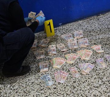 First image shows a police officer in black vest labeled POLICIA NACIONAL CIVIL standing in a room with shelves clothes and household items. Second image depicts an officer in black hooded jacket labeled DIPANDA INVESTIGACION CRIMINAL at a doorway with hanging clothes and blue walls. Third image features an officer in black clothing and vest labeled INTERPOL standing near a door with baskets and plastic items in a room with blue walls. Fourth image displays stacks of Guatemalan quetzale banknotes on the floor marked with evidence tag 1 next to a police officer in blue uniform wearing gloves pointing to the cash.