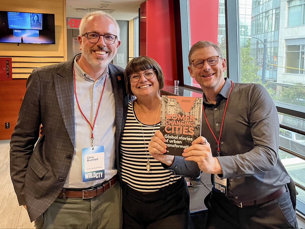 Three middle aged people in casual business attire—two men and one woman—pose for a photo at a conference.