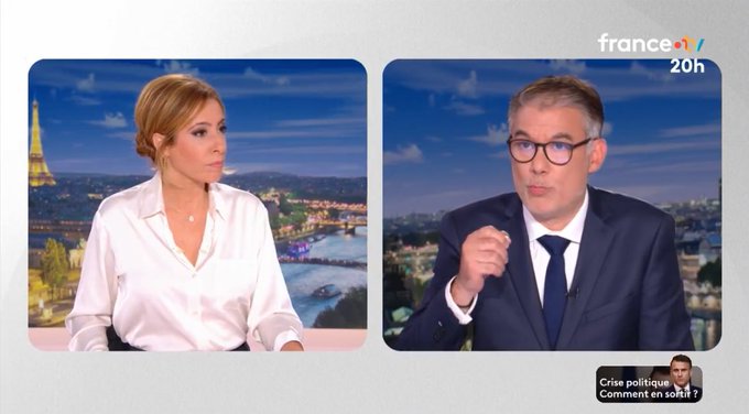 Split-screen television interview setup on France 2 channel with a woman in a white blouse wearing a necklace seated against a blue evening skyline featuring the Eiffel Tower and river, and a man in glasses, dark suit, and tie gesturing while speaking, with channel logo, program name Commentaire Politique, and date stamp visible at the bottom.