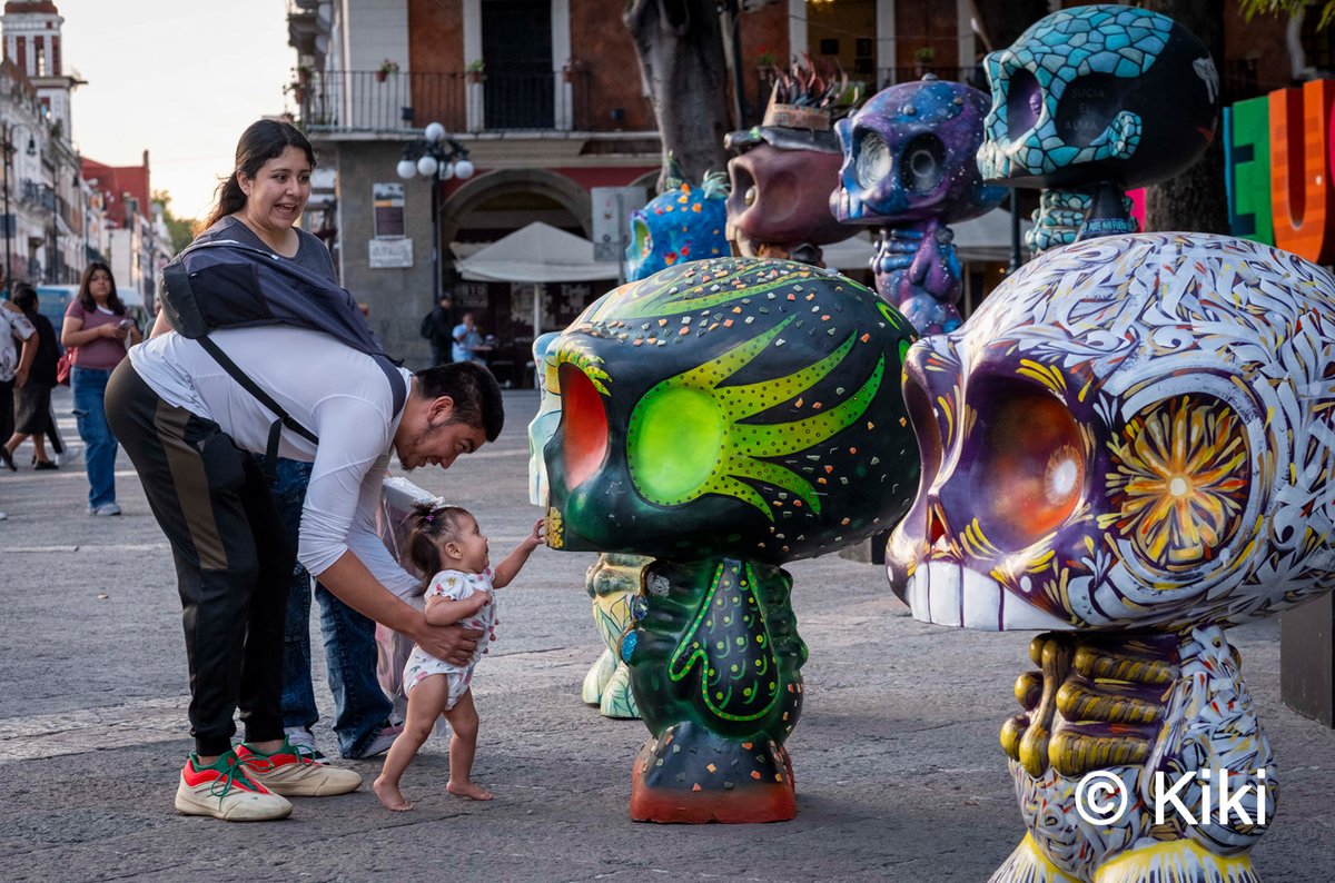 𝐂𝐚𝐥𝐚𝐯𝐞𝐫𝐚𝐬 𝐢𝐧𝐟𝐚𝐧𝐭𝐢𝐥𝐞𝐬 𝐩𝐚𝐫𝐚 𝐞𝐥 𝐃𝐢́𝐚 𝐝𝐞 𝐌𝐮𝐞𝐫𝐭𝐨𝐬.
22/10/25 En el corazón del Zócalo de Puebla, una niña descubre, de la mano de su padre, una calavera colorida hecha por artesanos locales. Así se hereda, desde la infancia, el amor por la cultura y