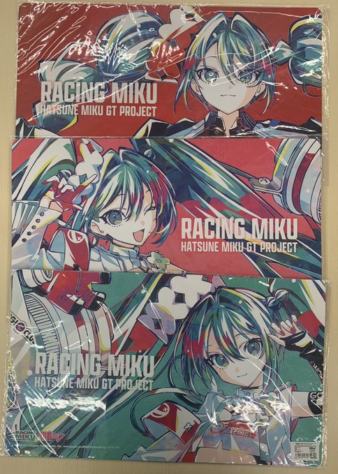 Three packaged multi desk mats displayed stacked. Top package in red with Racing Miku illustration showing green-haired character in racing outfit with gloves and headset. Middle package in red with similar character pose. Bottom package in green with character holding soccer ball in racing attire. Labels include Racing Miku Hatsune Miku GT Project.
