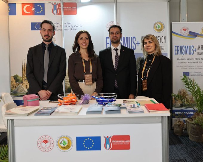 First image displays a group of four professionals standing behind a booth table at an exhibition. The booth features banners with Erasmus+ and ESC logos, Turkish and EU flags, promotional brochures, orange bags, and plants. A man and woman in business attire converse near the setup with Istanbul skyline imagery in the background. Second image shows two men at another booth with materials on Erasmus+ Youth Exchange, chairs, tables with documents, plants, and flags including Turkish and EU ones. The setting includes exhibition hall elements like lighting and neighboring booths.