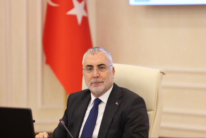 A man in a dark suit with a blue tie and glasses sits at a desk in an office with a Turkish flag on the wall behind him and a screen in the background. Another image shows a long conference table in a modern room with multiple people in formal attire seated around it including women in headscarves discussing with documents water bottles and microphones present and Turkish flags displayed. A third image depicts a similar conference setup with men and women in business suits at a wooden table with laptops papers and flags including a Turkish one in a formal meeting room.